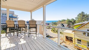 Une terrasse en bois, avec des chaises et une table, d’où l’on a vue sur un quartier résidentiel et l’océan.