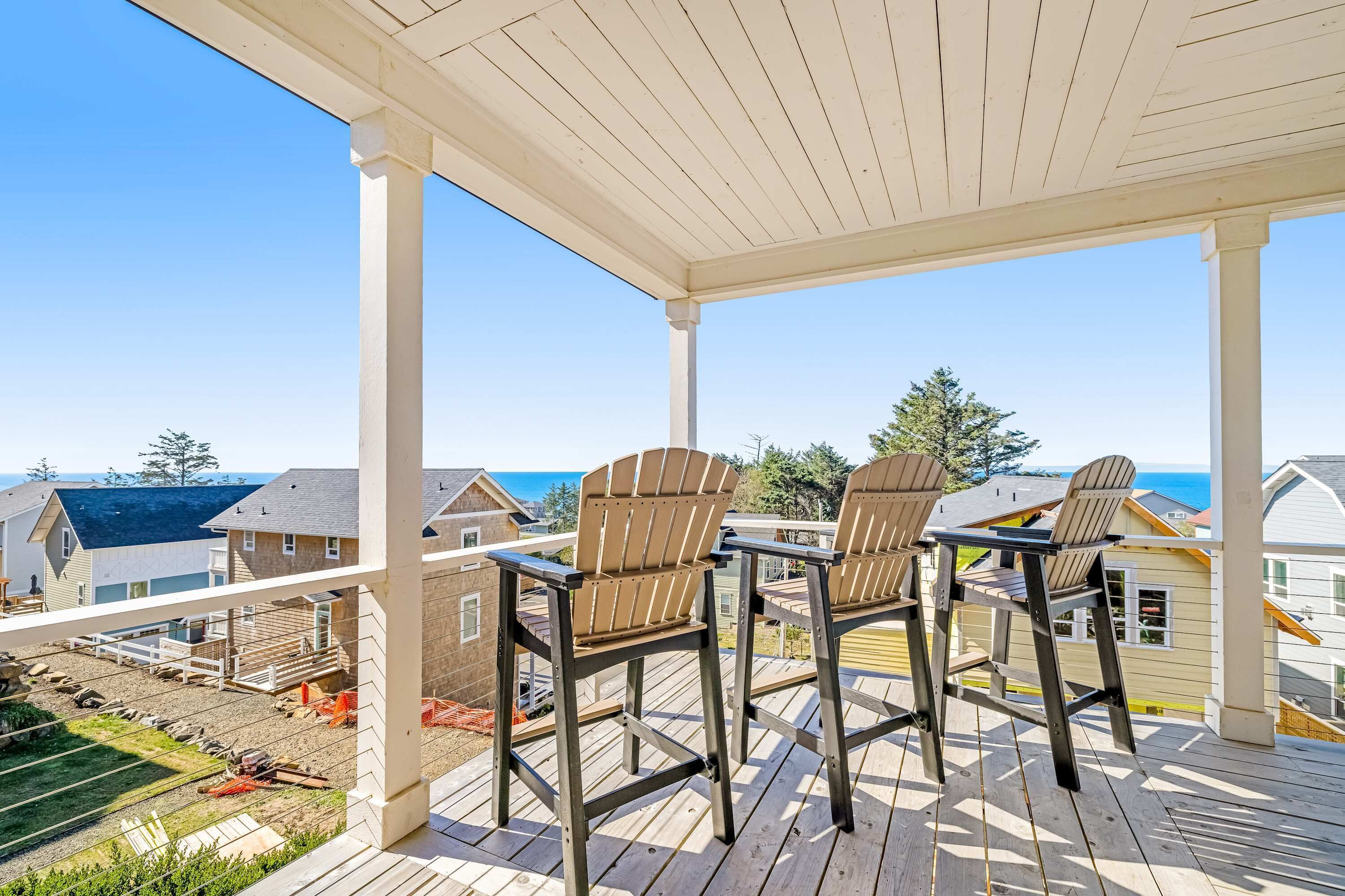 A covered outdoor deck with Adirondack chairs and a view of the ocean.