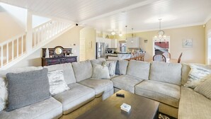 A spacious living room with a large sectional sofa, a dark coffee table, and a staircase leading to an upper level. - Family Home with Game Room WiFi Fireplace Private Hot Tub Walk to Beach (Lincoln City)