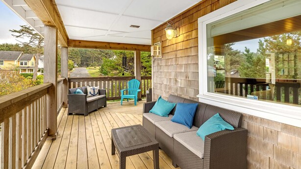 A covered deck with a wicker sofa, a small table, and a blue chair. - Family Home with Game Room WiFi Fireplace Private Hot Tub Walk to Beach (Lincoln City)