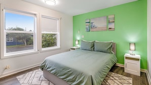 A bedroom with a large bed, two bedside tables with lamps, a green wall, and a window with a view of the outdoors. - Ocean view home with pool table and fast WiFi steps to beach shops and eateries (Lincoln City)
