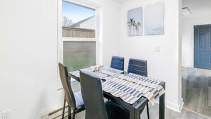 A dining area with a table set for six, surrounded by chairs, a window with a view of a backyard, and a door leading to another room. - Ocean view home with pool table and fast WiFi steps to beach shops and eateries (Lincoln City)