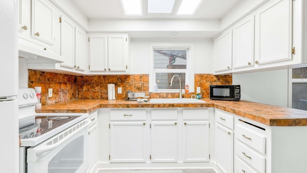 A modern kitchen with white cabinets, a granite countertop, a built-in oven, and a microwave. - Ocean view home with pool table and fast WiFi steps to beach shops and eateries (Lincoln City)