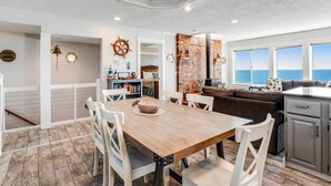 Une cuisine moderne avec une table en bois, des chaises blanches et un mur de fond en briques apparentes.
