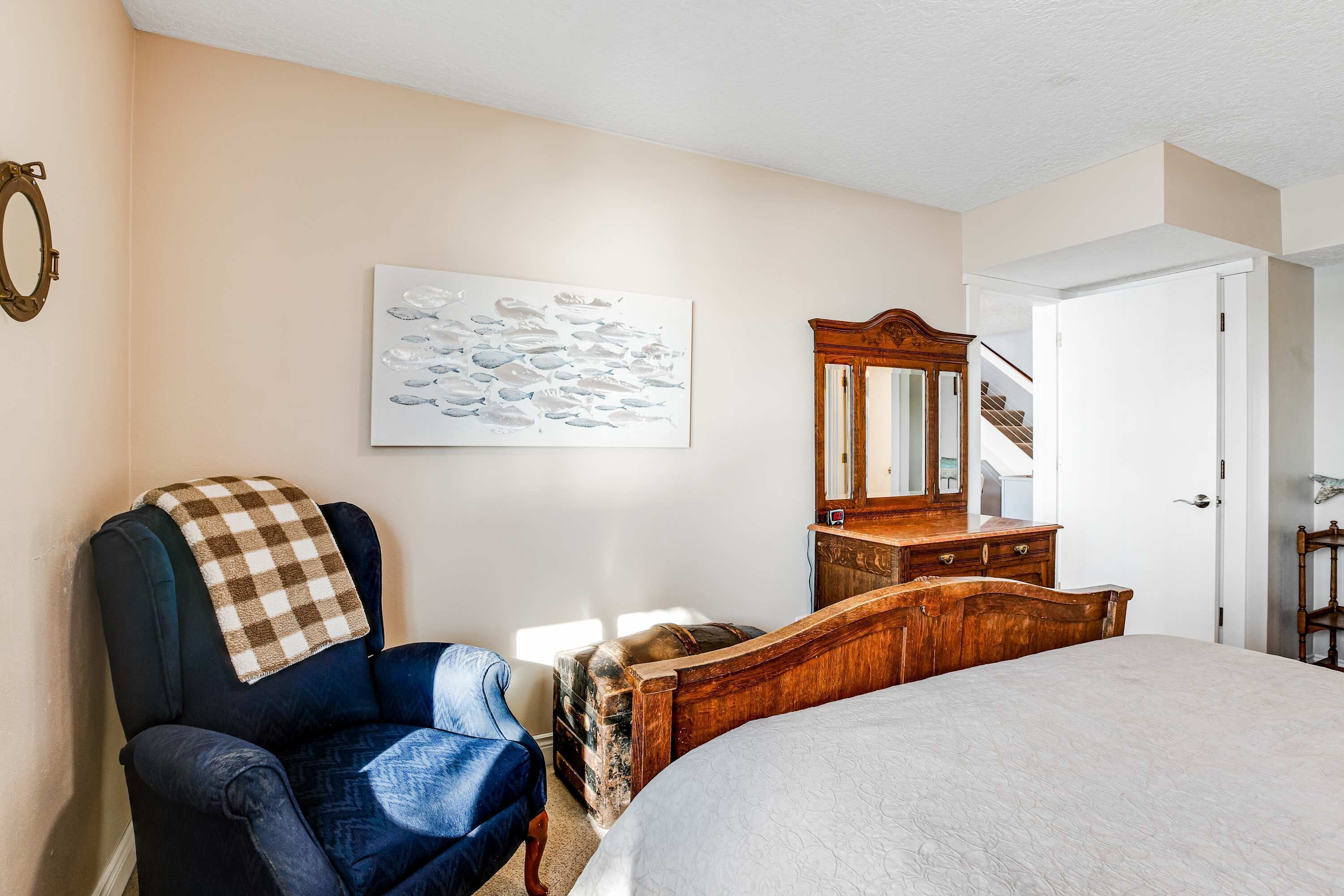 A bedroom with a bed, a chair, a dresser, a mirror, and a painting on the wall.