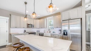 Uma cozinha moderna com uma ilha grande, eletrodomésticos de aço inoxidável e iluminação pendente.