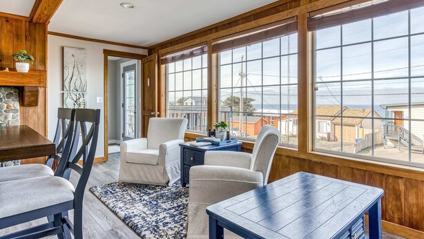 A sunroom with a wooden ceiling, large windows, a dining table, chairs, and a small side table. - Ocean view home 1 block from the beach with hot tub deck and fireplace (Lincoln City)