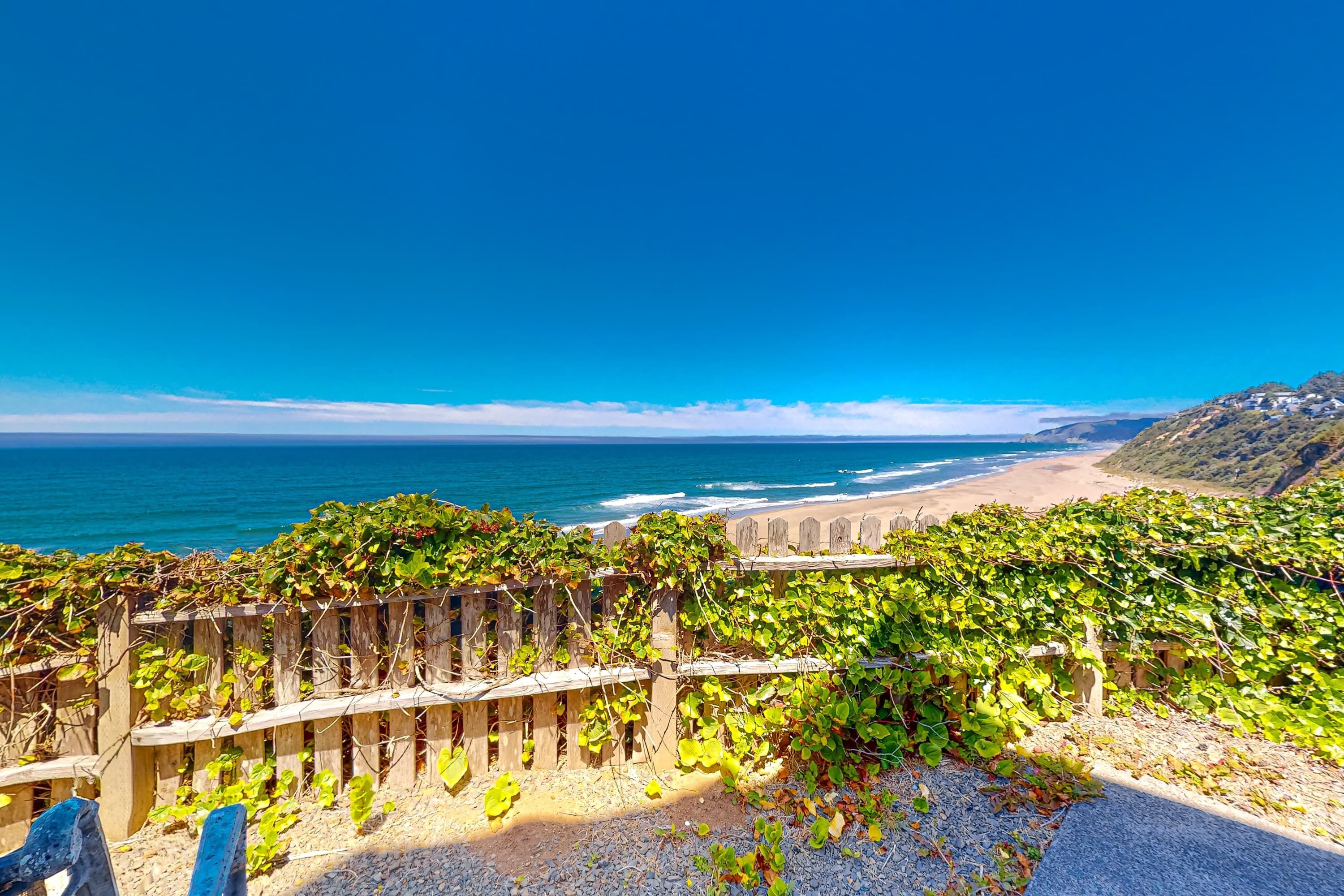 A coastal view with a wooden fence, beach, and ocean.
