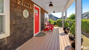 A wooden house with a red door, numbered 2704, and a porch with two red Adirondack chairs. - Cottage de la Mer House in Lincoln City with serene porch walk to the beach (Lincoln City)
