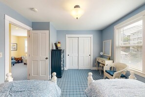 Ein Schlafzimmer mit zwei Betten, einem Schminktisch, einem Stuhl, einem Schreibtisch und einer Tür zu einem anderen Raum.