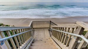 Een houten trap die naar een strand leidt, met uitzicht op de oceaan.