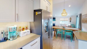 Una cocina moderna con cafetera integrada, refrigerador y un comedor con sillas color turquesa.