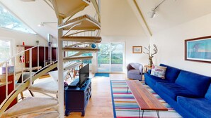 Ein modernes Wohnzimmer mit Wendeltreppe, einem blauen Sofa, einem Holztisch und einem Fernseher auf einem Schrank.