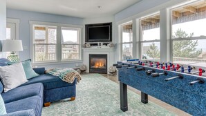 A spacious living room with a foosball table, a fireplace, and large windows offering a view of the outdoors. - Ocean view home with hot tub game room furnished deck and fireplaces (Lincoln City)