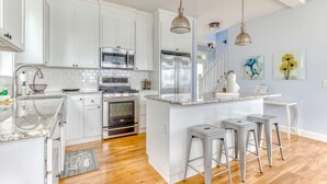 A modern kitchen with white cabinets, stainless steel appliances, and a central island with bar stools. - Ocean view home with hot tub game room furnished deck and fireplaces (Lincoln City)