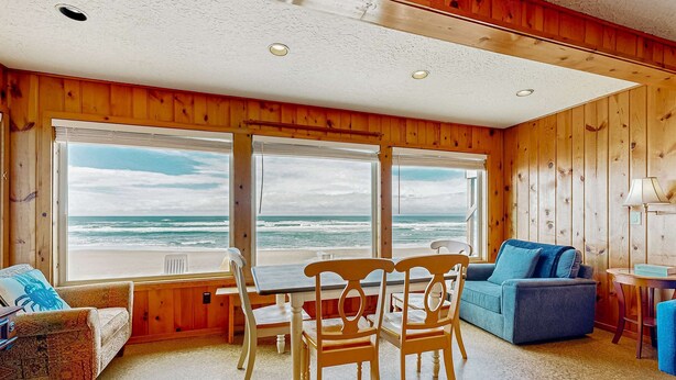 Een kamer met houten wanden, een groot raam met uitzicht op zee, een blauwe bank, een houten tafel en een stoel.