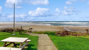 Een picknickplaats aan het strand, met een houten tafel en een wandelpad dat naar de oceaan leidt.