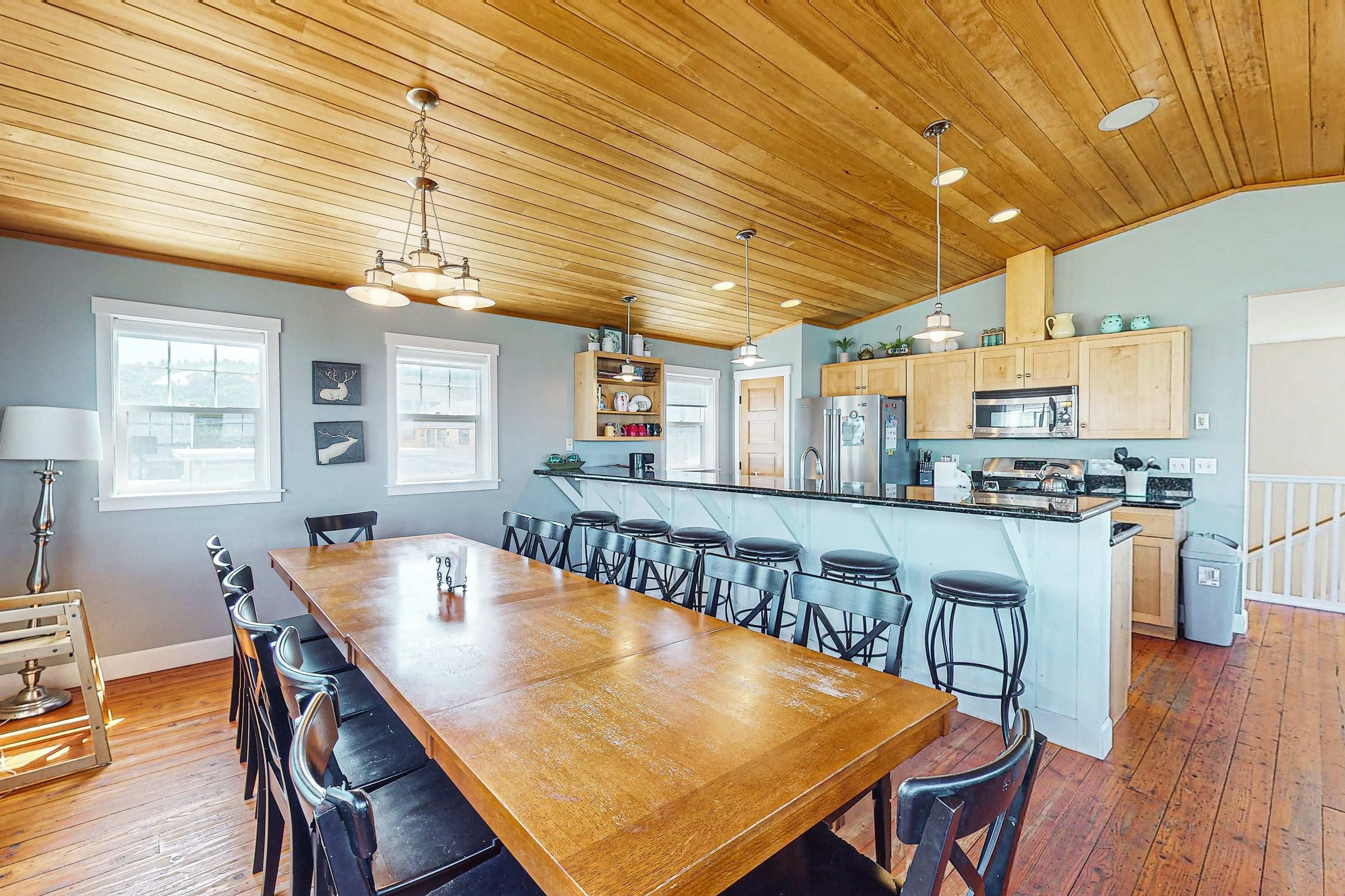 A spacious kitchen with a long wooden table, bar stools, and a central island with a sink and microwave.