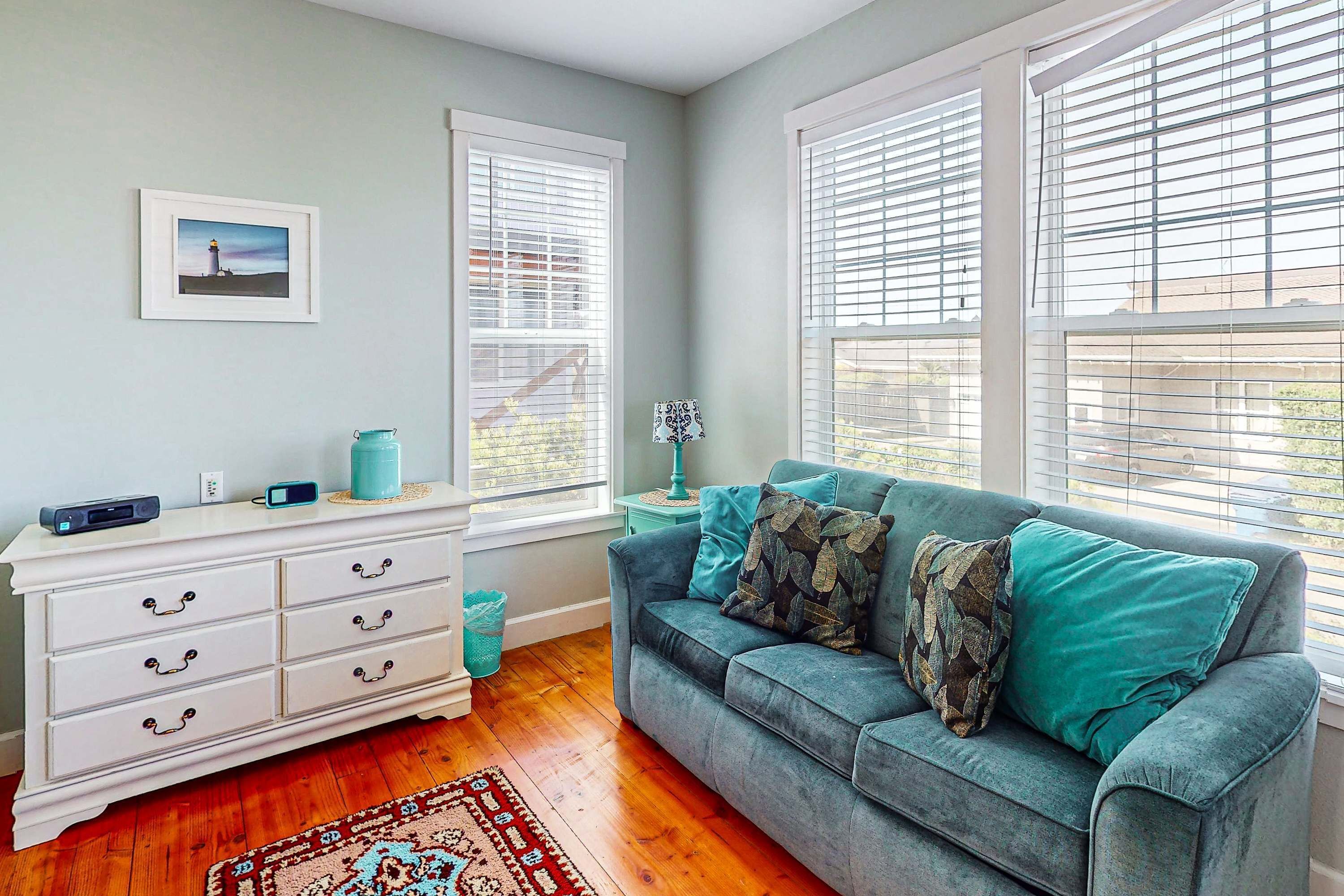 A room with a grey sofa, a white dresser, and a window with blinds.