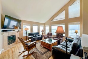 A spacious living room with a fireplace, leather sofas, a coffee table, and large windows overlooking the sea. - Beautiful home on the ocean with beach views deck bbq WiFi and streaming (Lincoln City)