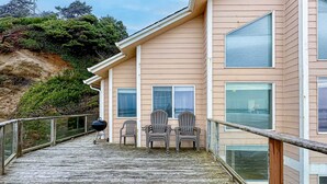 Une maison située sur la côte, dotée d’un balcon, de trois fauteuils Adirondack et d’un barbecue.