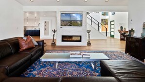 A spacious living room with a fireplace, a large TV mounted above it, and a view of the outdoors through a window. - Spacious home with ocean view enclosed yard fireplace hut tub washer and dryer (Lincoln City)