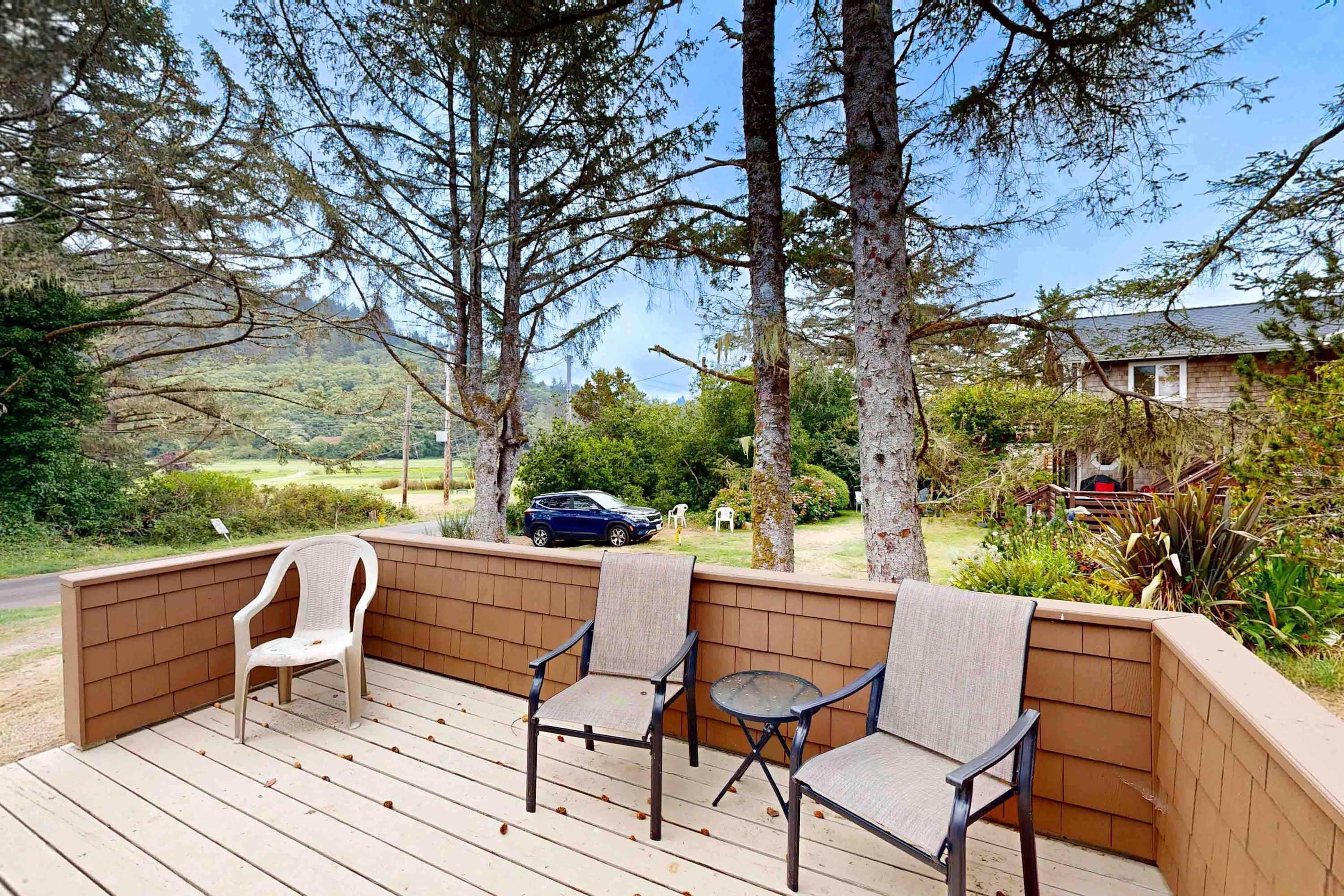 Een houten terras met een zithoek, inclusief stoelen en een tafel, omringd door bomen en uitzicht op een woonwijk.