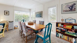 A dining area with a wooden table, patterned chairs, a bookshelf with books, and framed pictures on the walls.