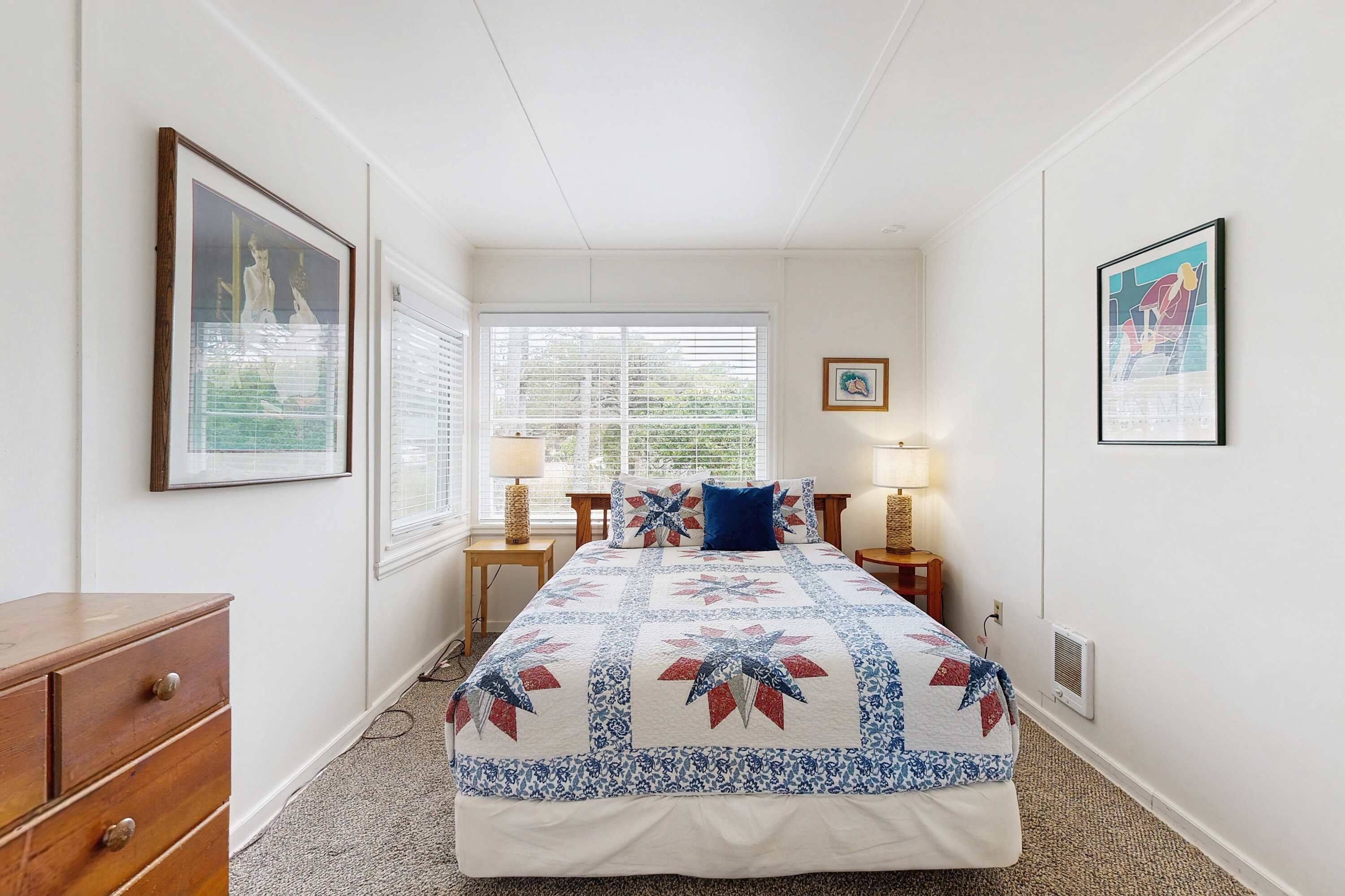 Une chambre à coucher avec un grand lit, deux tables de chevet avec des lampes, une commode et des œuvres d’art encadrées accrochées aux murs.