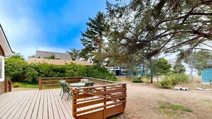 A wooden deck with a fence, outdoor seating, and a view of a building and trees.