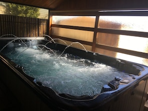 Un bain à remous avec jets d’eau, une terrasse en bois et une vue à travers une fenêtre en verre dépoli.