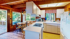A wooden cabin kitchen with a central island, white cabinets, and a large window overlooking a forest. - Dog friendly cabin with ocean view fast WiFi fireplace and washer dryer (Otis)