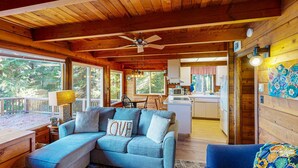 A cozy cabin interior with a wooden ceiling, a blue sofa with a 'LOVE' pillow, a dining area, and a kitchen. - Dog friendly cabin with ocean view fast WiFi fireplace and washer dryer (Otis)