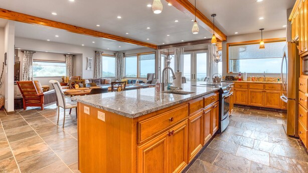 A spacious kitchen with wooden cabinets, a large island, and a stone-tiled floor.