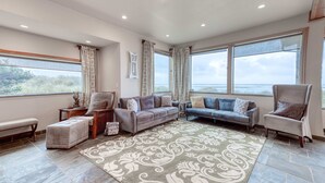 A spacious living room with a large window, a grey sofa, a blue sofa, and a beige armchair.