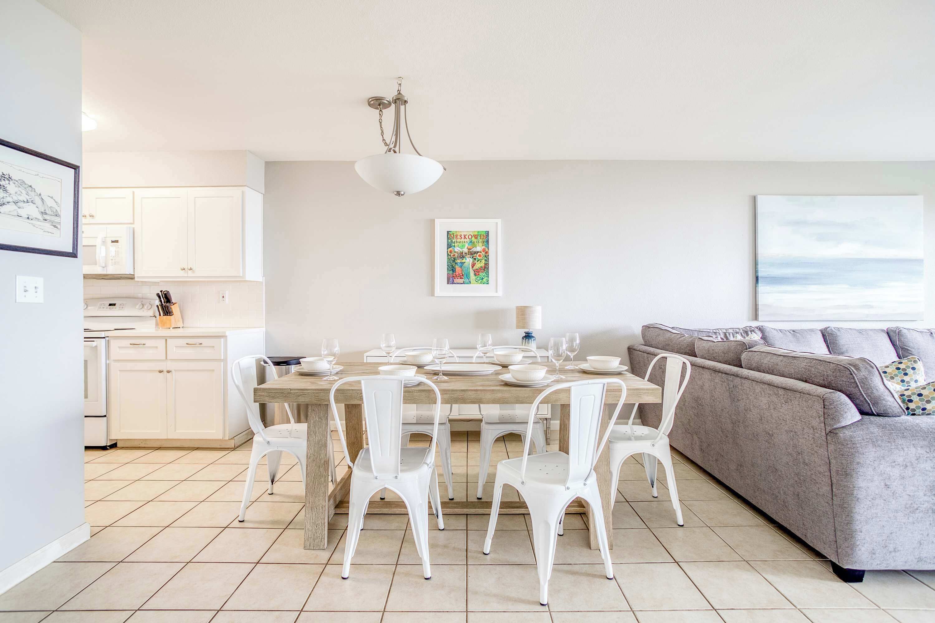 A modern kitchen with white cabinets, a dining table set for six, and a grey sofa in the living area.