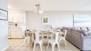 Une cuisine moderne avec des meubles blancs, une table à manger dressée pour six personnes et un canapé gris dans l’espace salon.