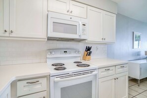 Une cuisine avec des meubles blancs, un four à micro-ondes, une cuisinière et un bloc à couteaux.