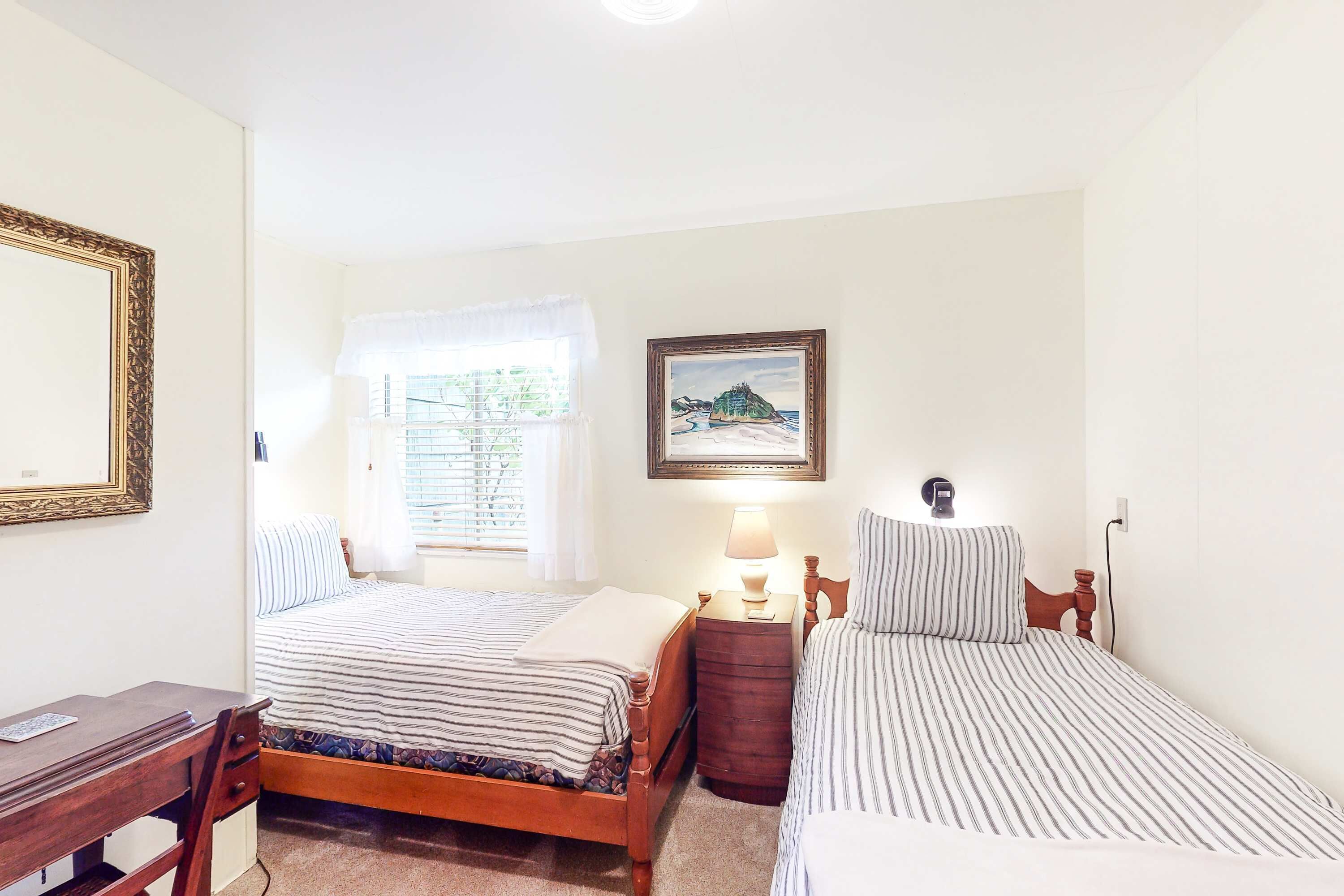 A bedroom with two beds, a desk, and a window with curtains.