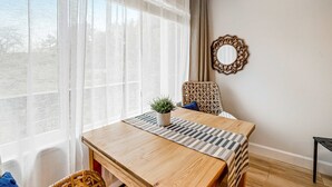 A room with a wooden table, a woven mat, a potted plant, a wicker chair, and a mirror on the wall.
