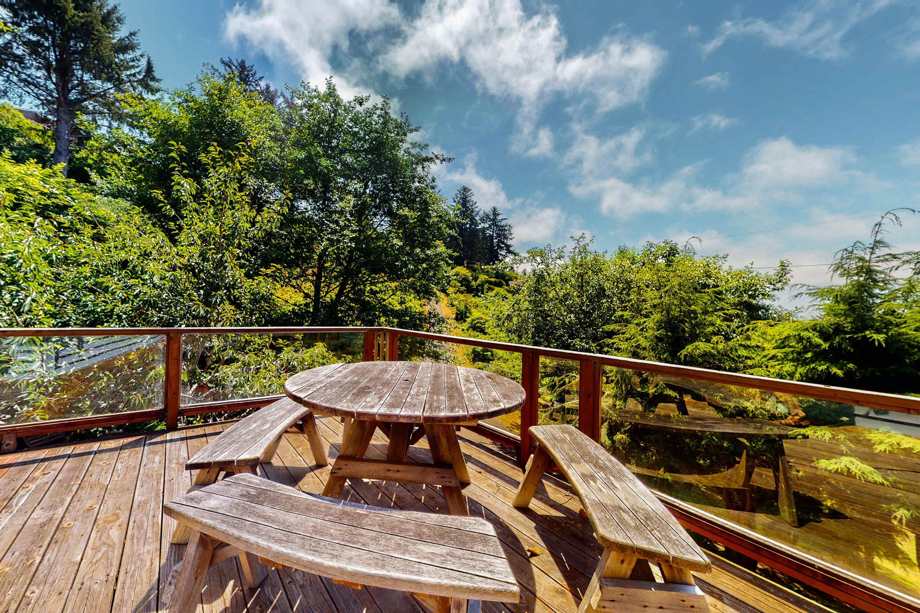 A wooden deck with a picnic table and benches, surrounded by lush greenery and trees.