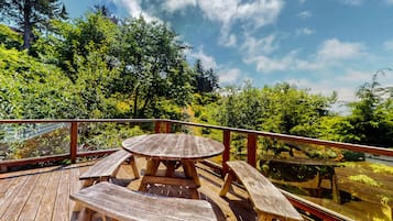A wooden deck with a picnic table and benches, surrounded by lush greenery and trees.