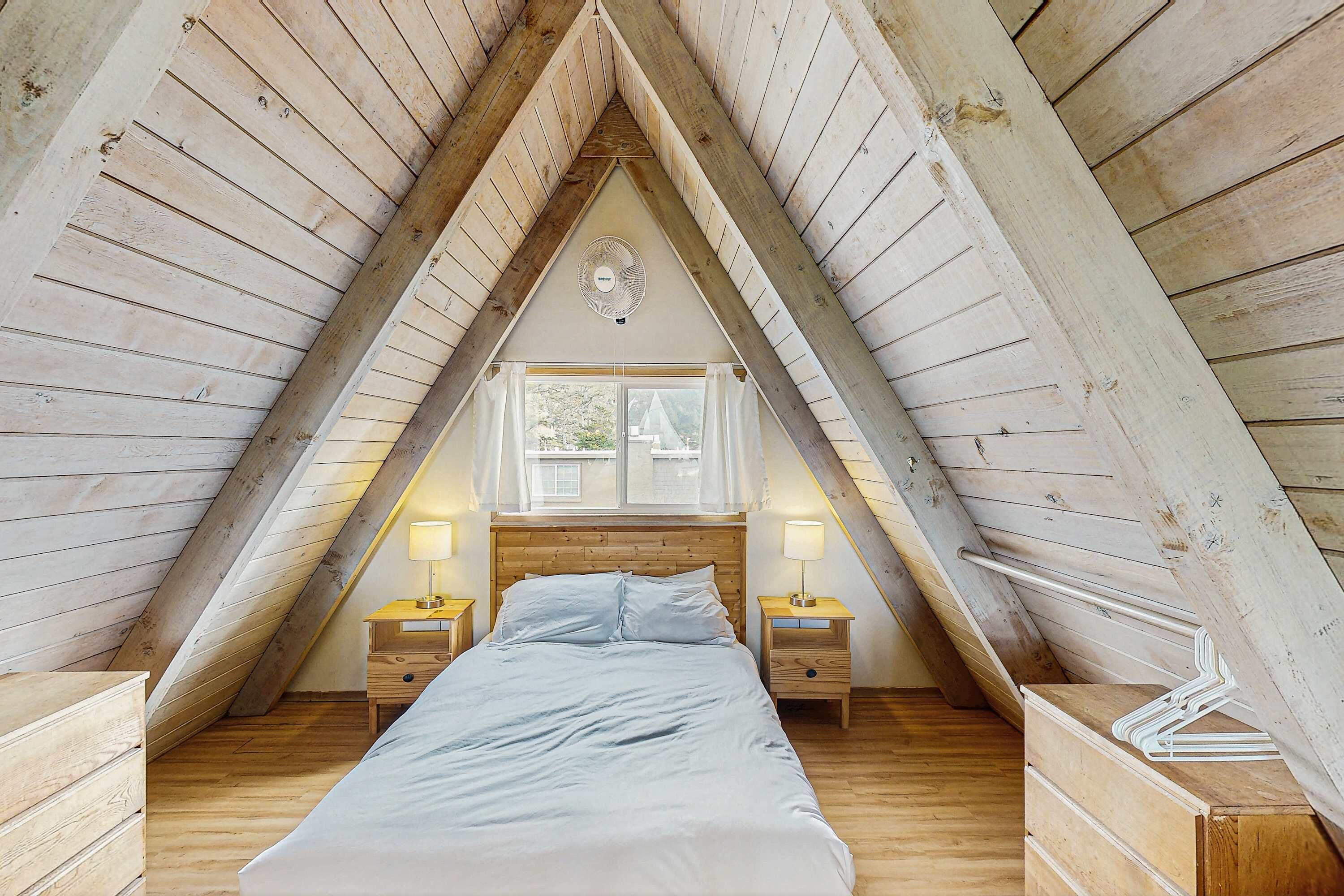 Une chambre avec un plafond en pente, des murs en bois, un lit, deux tables de chevet avec des lampes et une fenêtre.