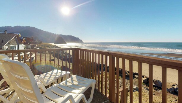 Vista sulla spiaggia dal balcone, con sedie di plastica bianca e ringhiera in legno.