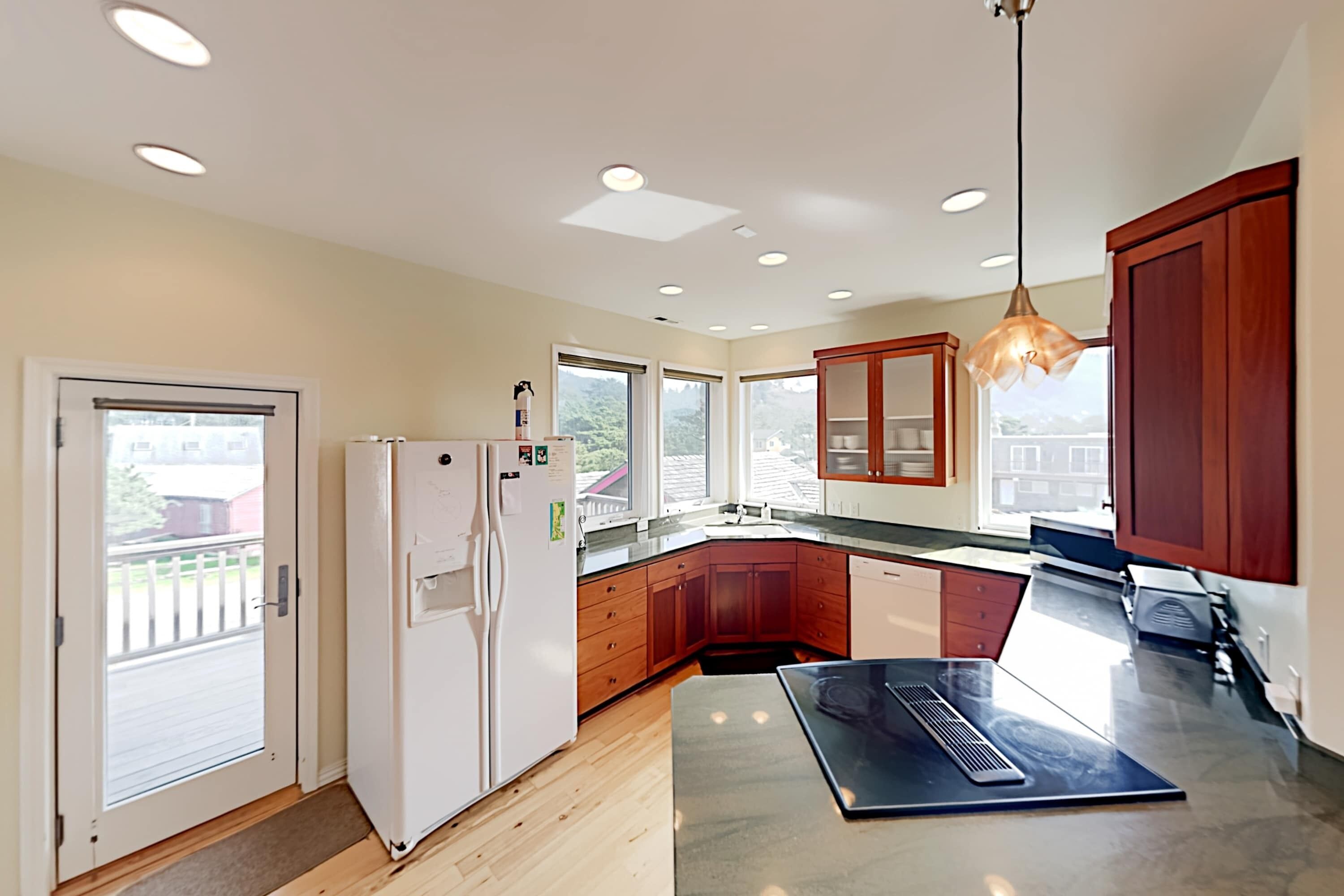 A modern kitchen with wooden cabinets, a white refrigerator, and a large island with a built-in stove.