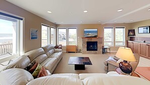 Ein geräumiges Wohnzimmer mit einer großen Couch, einem Kamin und Blick ins Freie.
