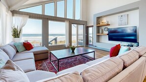 Una sala de estar moderna con un ventanal que da a una playa, un televisor de pantalla plana y una zona de estar acogedora.