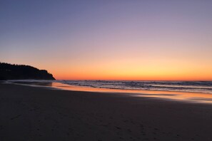 A beach at sunset with a calm sea and a forested hill in the background. - Oceanfront 2nd floor condo with river ocean views balcony (Neskowin)