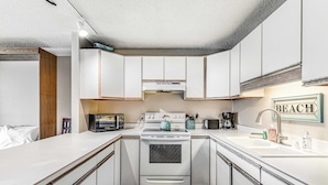 A compact kitchen with white cabinets, a stove, and a sink. - Oceanfront 2nd floor condo with river ocean views balcony (Neskowin)