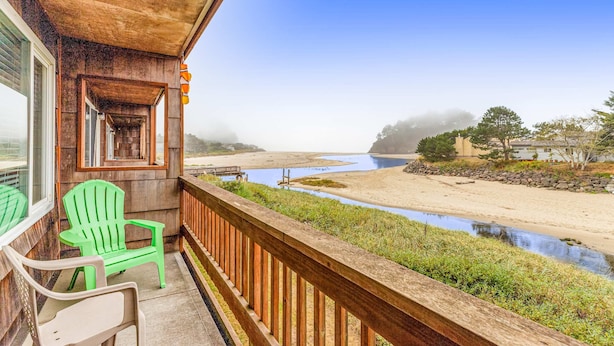 A wooden balcony with two green Adirondack chairs, overlooking a beach and a river. - Oceanfront 2nd floor condo with river ocean views balcony (Neskowin)